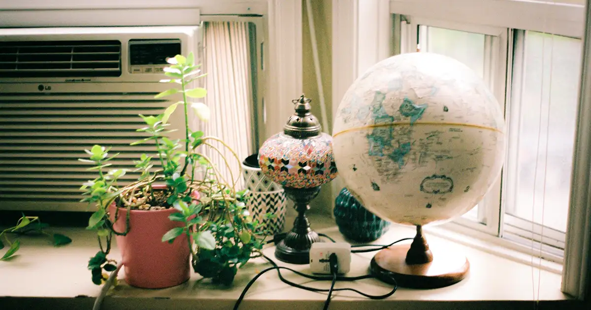 A window AC tries to cool a library where a plant and globe sit.